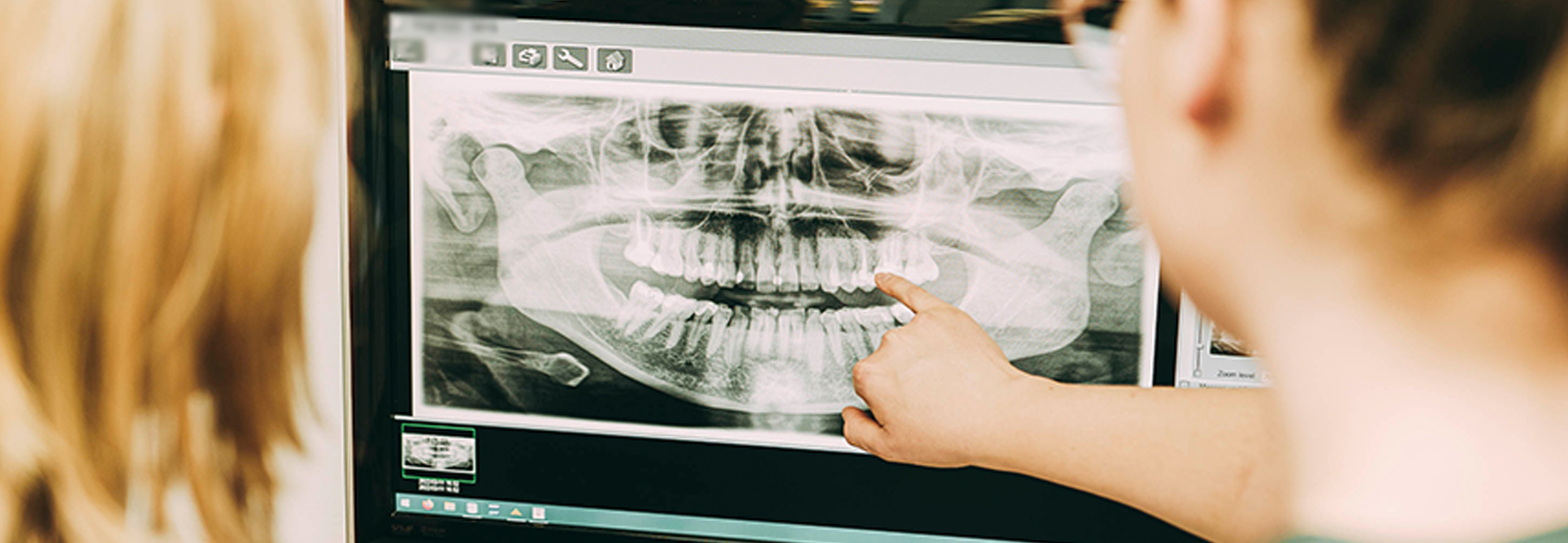 Zahnärztin Ricarda Richter zeigt auf einen Bildschirm in Ihrer Zahnarztpraxis, auf dem ein Röntgenbild von Zähnen gezeigt wird.